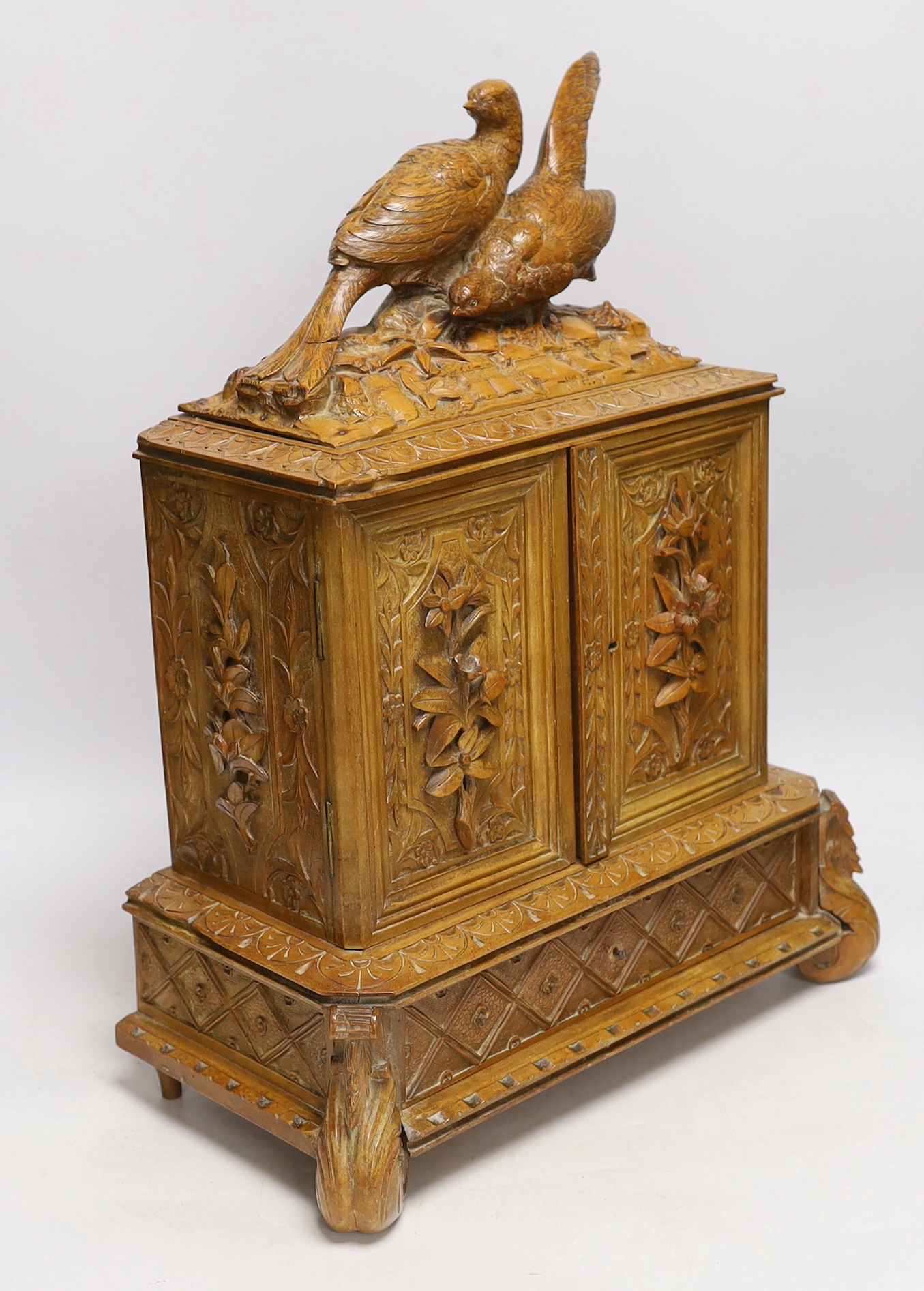 A late 19th century Black Forest carved wooden two door table top cabinet, interior with fitted drawers, surmounted with two pheasants, 51cm high
